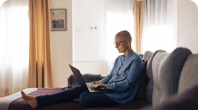 Person using laptop while sitting on a couch in a cozy room.